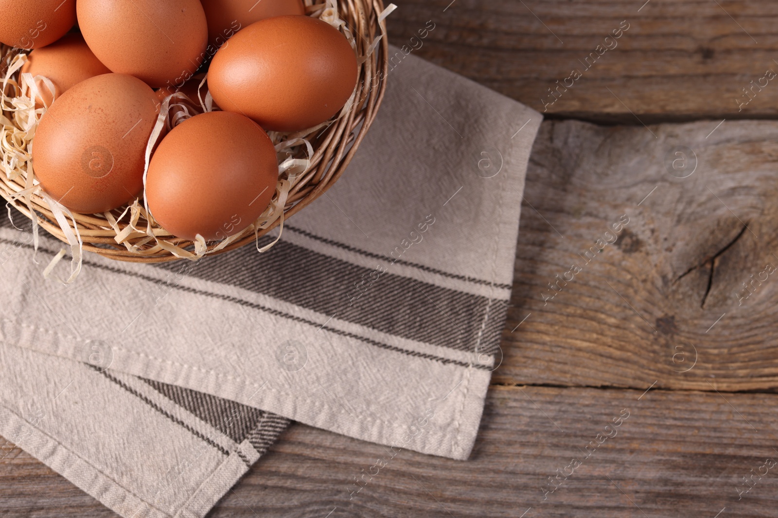 Photo of Wicker basket with fresh eggs on wooden table, top view. Space for text