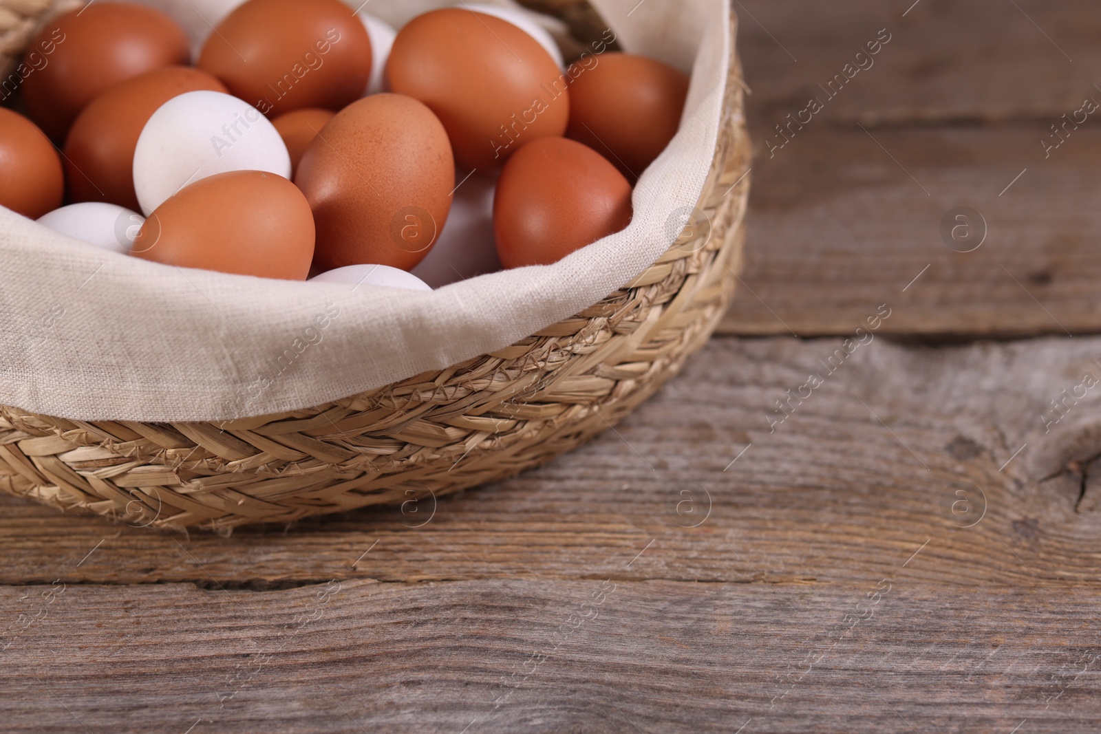 Photo of Wicker basket with fresh eggs on wooden table, closeup. Space for text