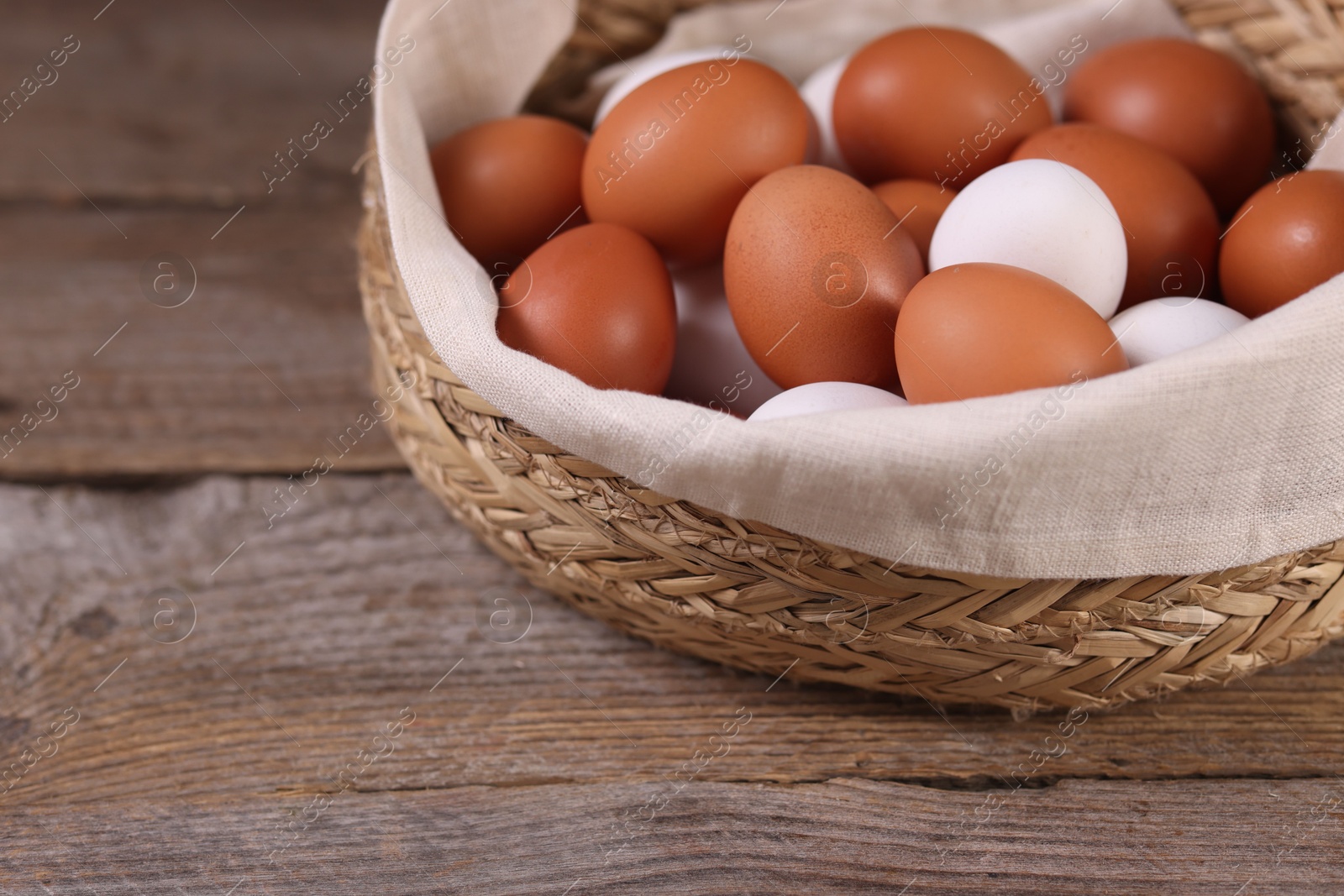 Photo of Wicker basket with fresh eggs on wooden table, closeup. Space for text