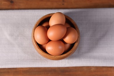 Photo of Fresh eggs in bowl on wooden table, top view