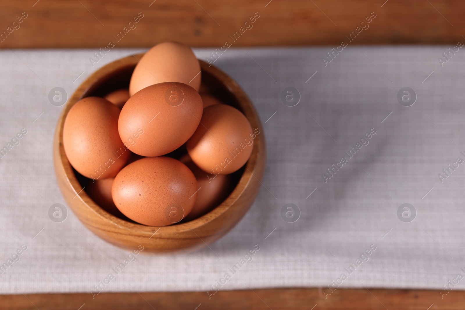 Photo of Fresh eggs in bowl on wooden table, closeup. Space for text