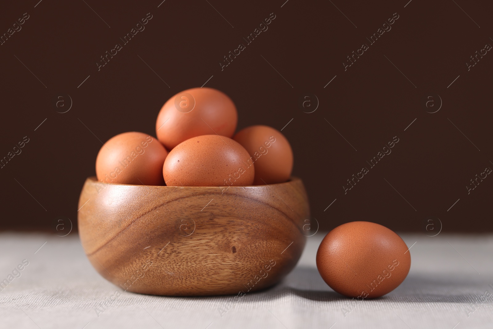 Photo of Fresh eggs in bowl on table against brown background, closeup