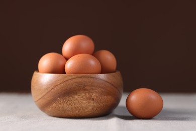 Photo of Fresh eggs in bowl on table against brown background, closeup