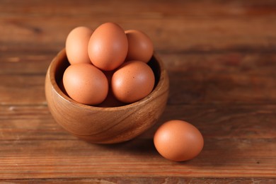 Photo of Fresh eggs in bowl on wooden table, closeup