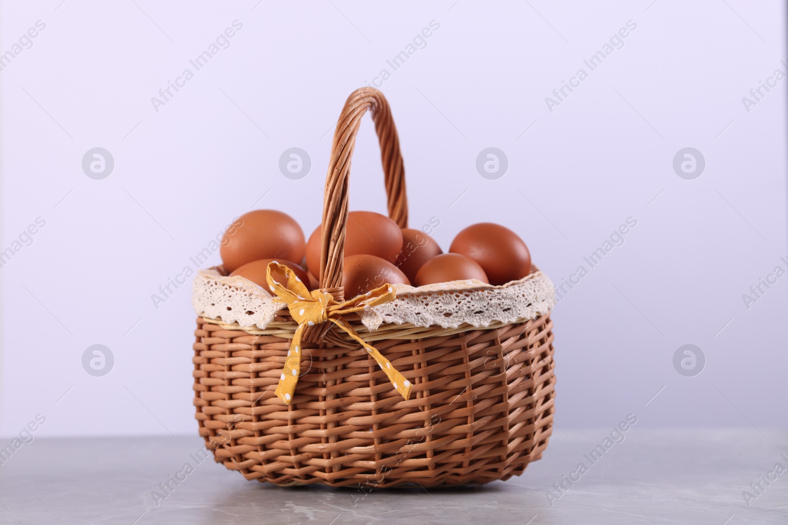 Photo of Wicker basket with fresh eggs on grey marble table against white background, closeup