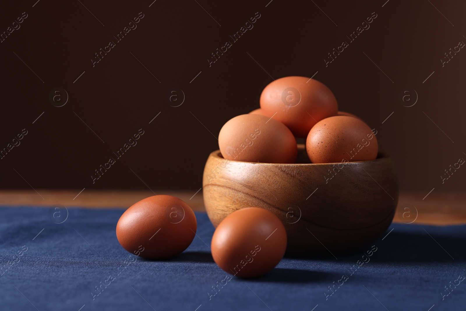 Photo of Fresh eggs and bowl on table against brown background, closeup