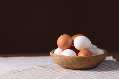 Photo of Fresh eggs in bowl on table against brown background, closeup. Space for text