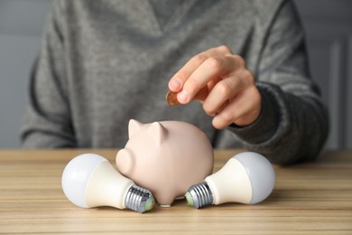 Photo of Man putting coin into piggy bank at wooden table, closeup. Energy saving concept