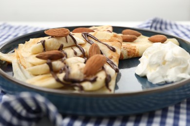 Photo of Delicious crepes with chocolate sauce, almonds and whipped cream on table, closeup