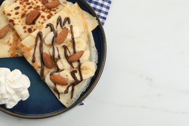 Photo of Delicious crepes with chocolate sauce, almonds and whipped cream on white table, top view. Space for text