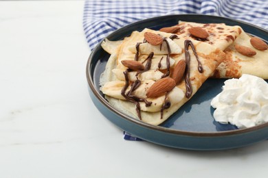 Photo of Delicious crepes with chocolate sauce, almonds and whipped cream on white table, closeup