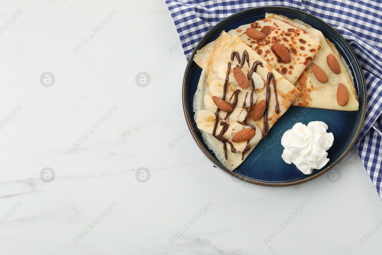 Photo of Delicious crepes with chocolate sauce, almonds and whipped cream on white table, top view. Space for text