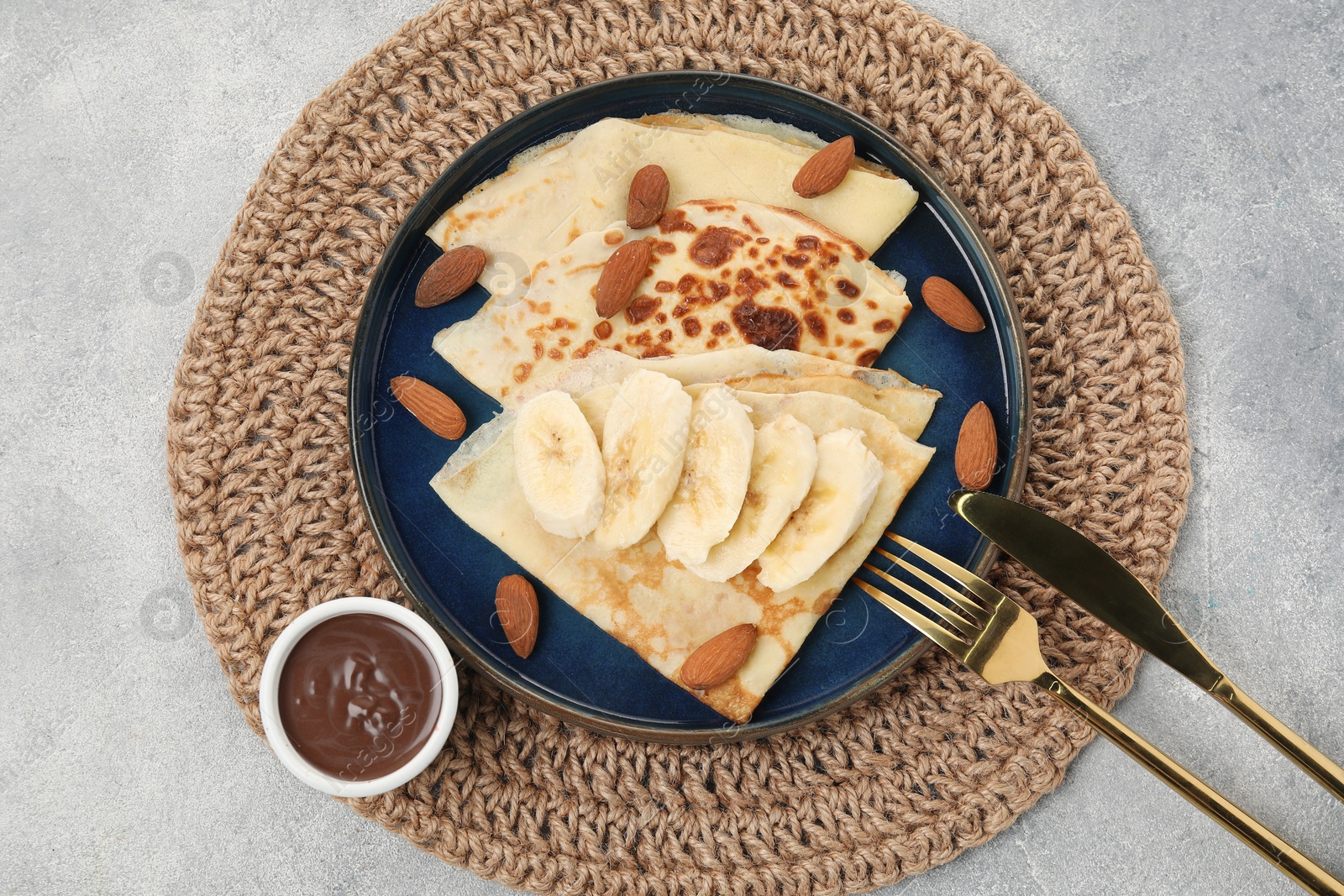 Photo of Delicious crepes with banana and almonds served on grey table, top view