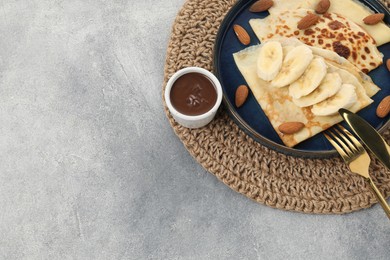 Photo of Delicious crepes with banana and almonds served on grey table, above view. Space for text