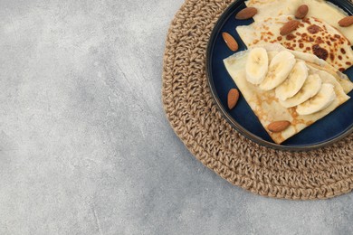 Delicious crepes with banana and almonds on grey table, top view. Space for text