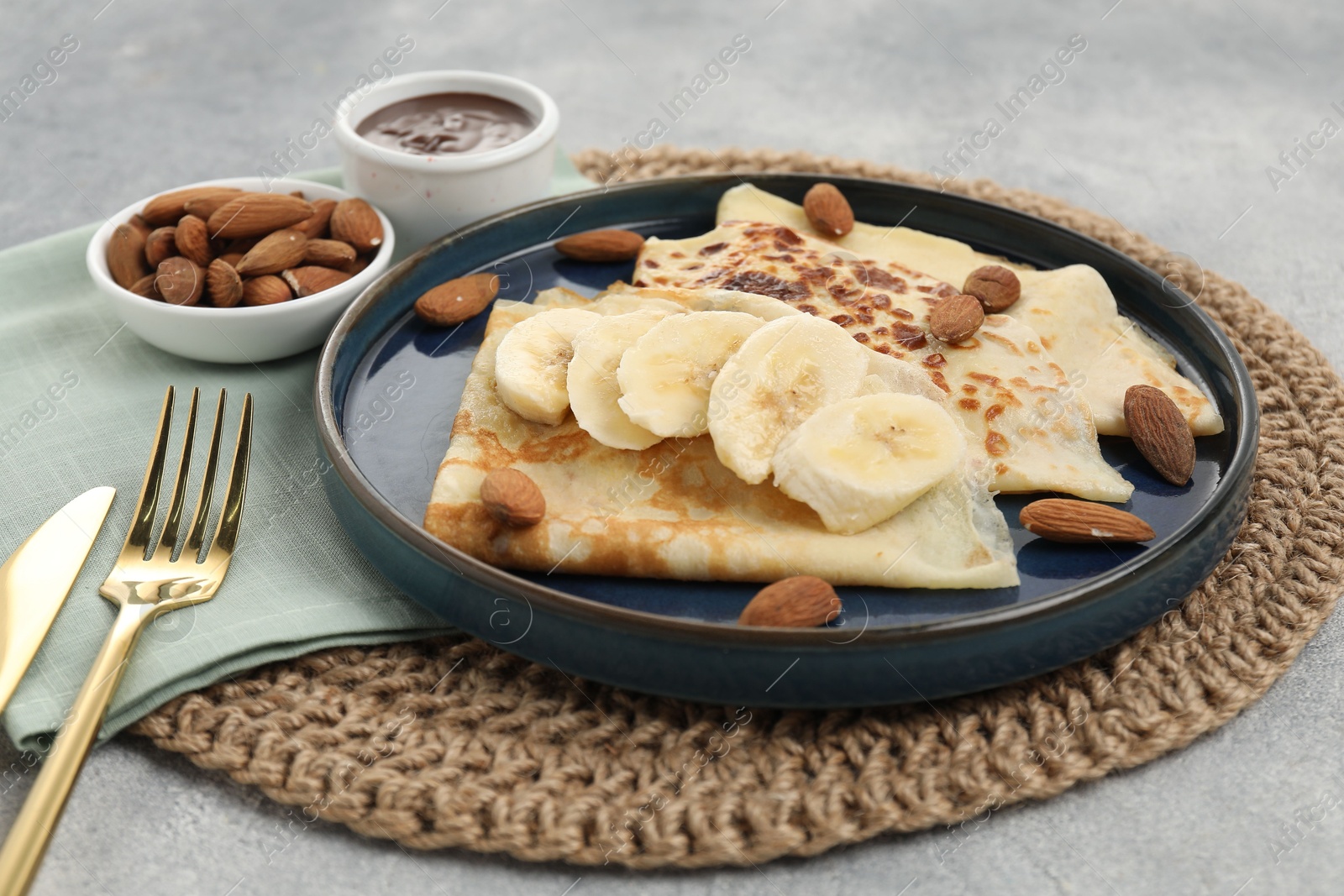 Photo of Delicious crepes with banana and almonds served on grey table, closeup