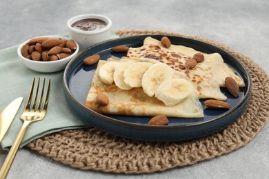 Delicious crepes with banana and almonds served on grey table, closeup