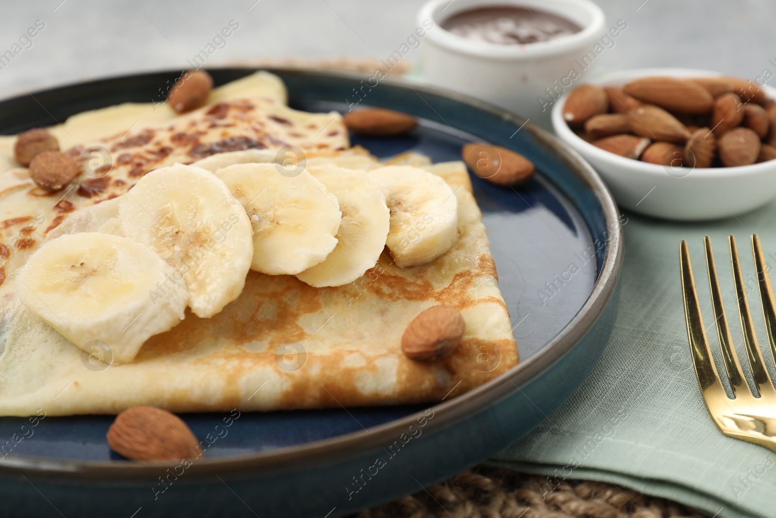 Photo of Delicious crepes with banana and almonds served on grey table, closeup