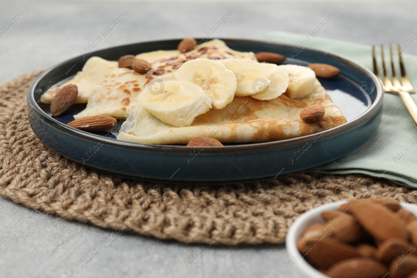 Photo of Delicious crepes with banana and almonds on grey table, closeup