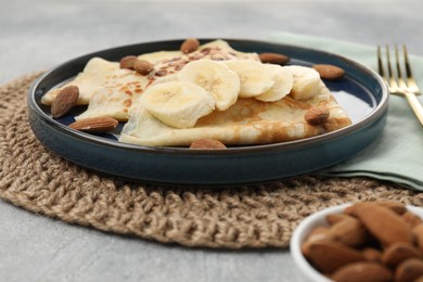 Delicious crepes with banana and almonds on grey table, closeup