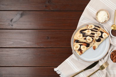 Delicious crepes with chocolate sauce, banana and almonds served on wooden table, flat lay. Space for text