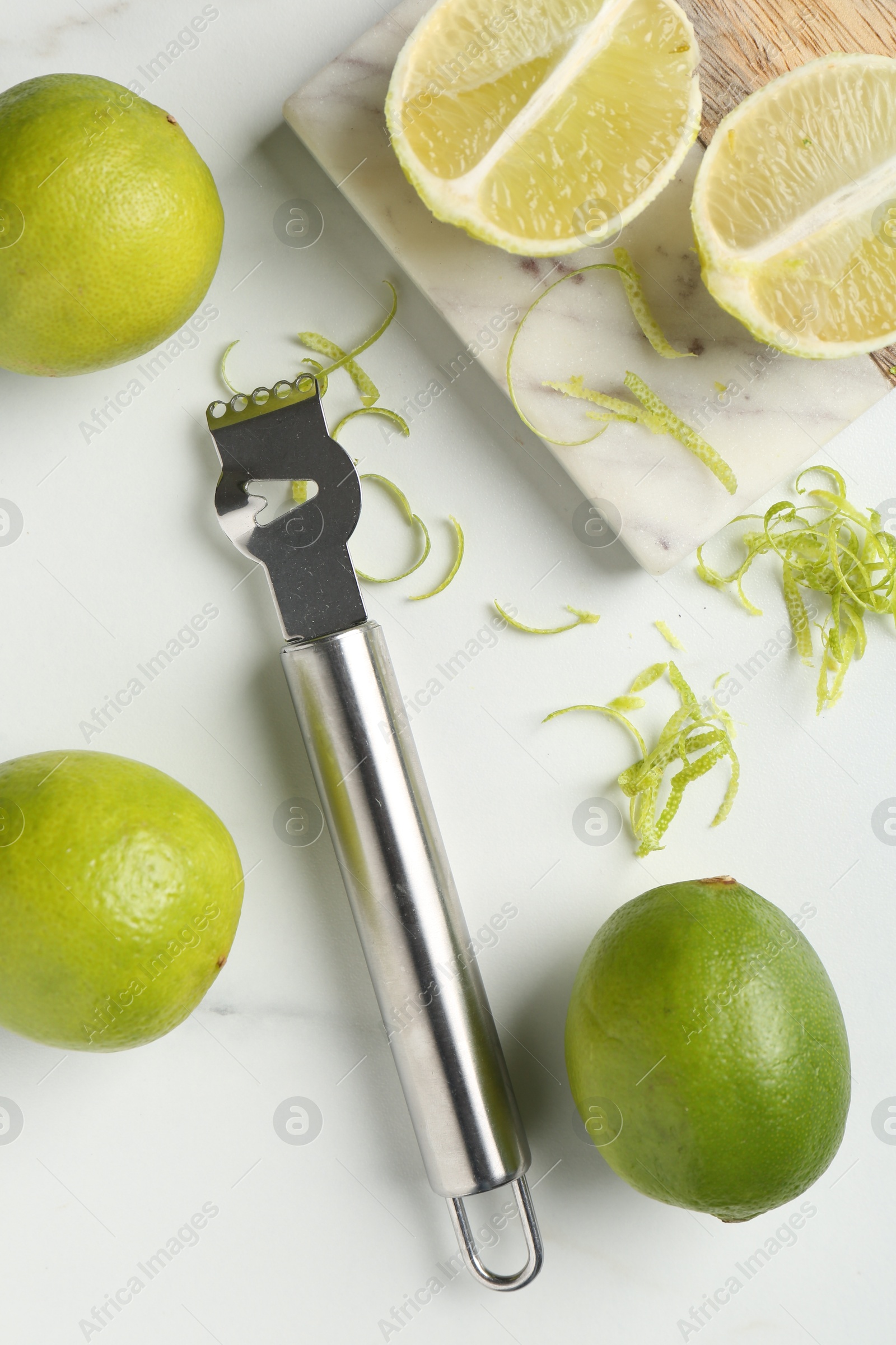 Photo of Lime zest, fresh fruits and zester tool on white marble table, flat lay