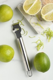 Photo of Lime zest, fresh fruits and zester tool on white marble table, flat lay