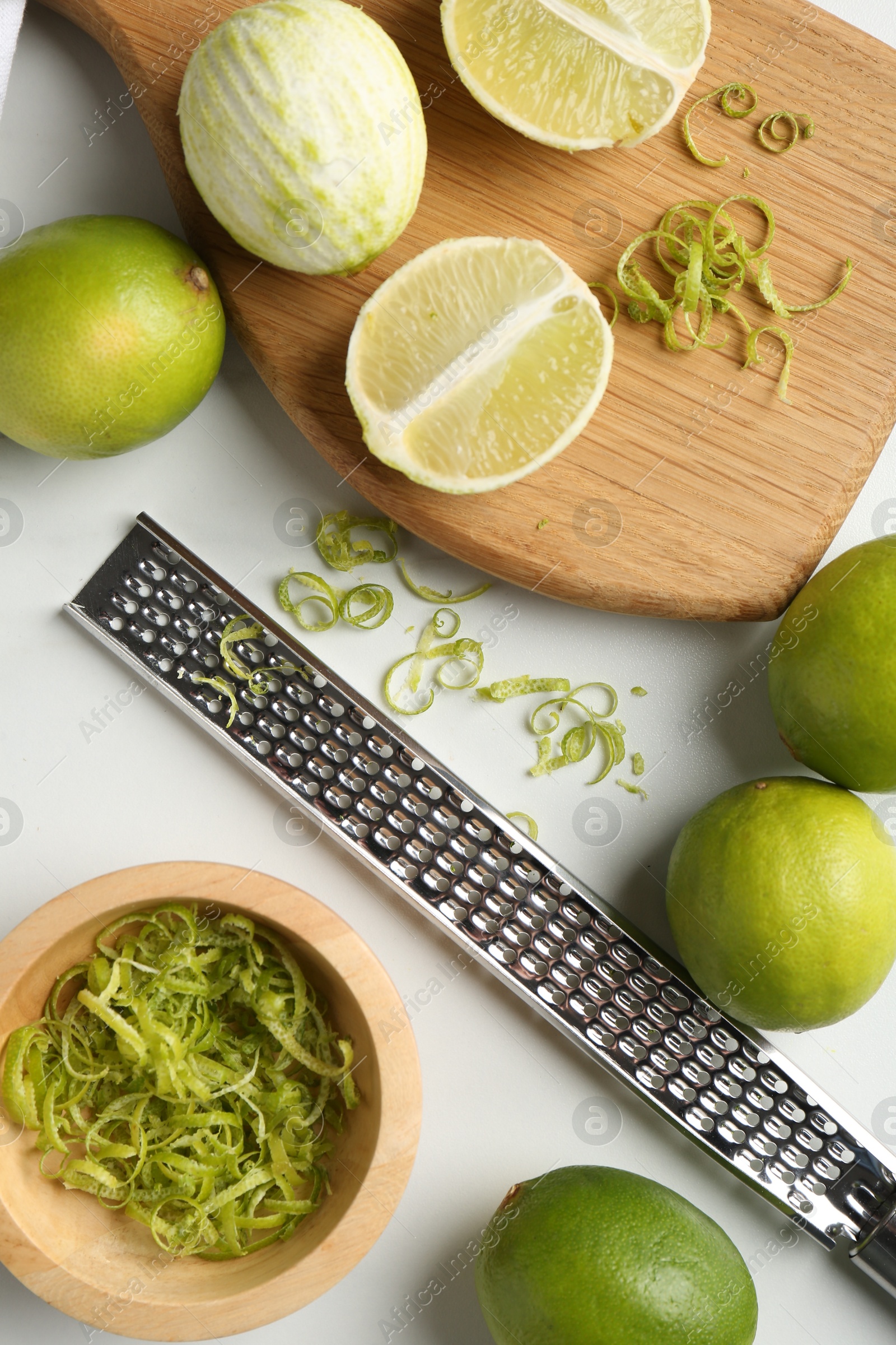 Photo of Lime zest, fresh fruits and grater on white marble table, flat lay