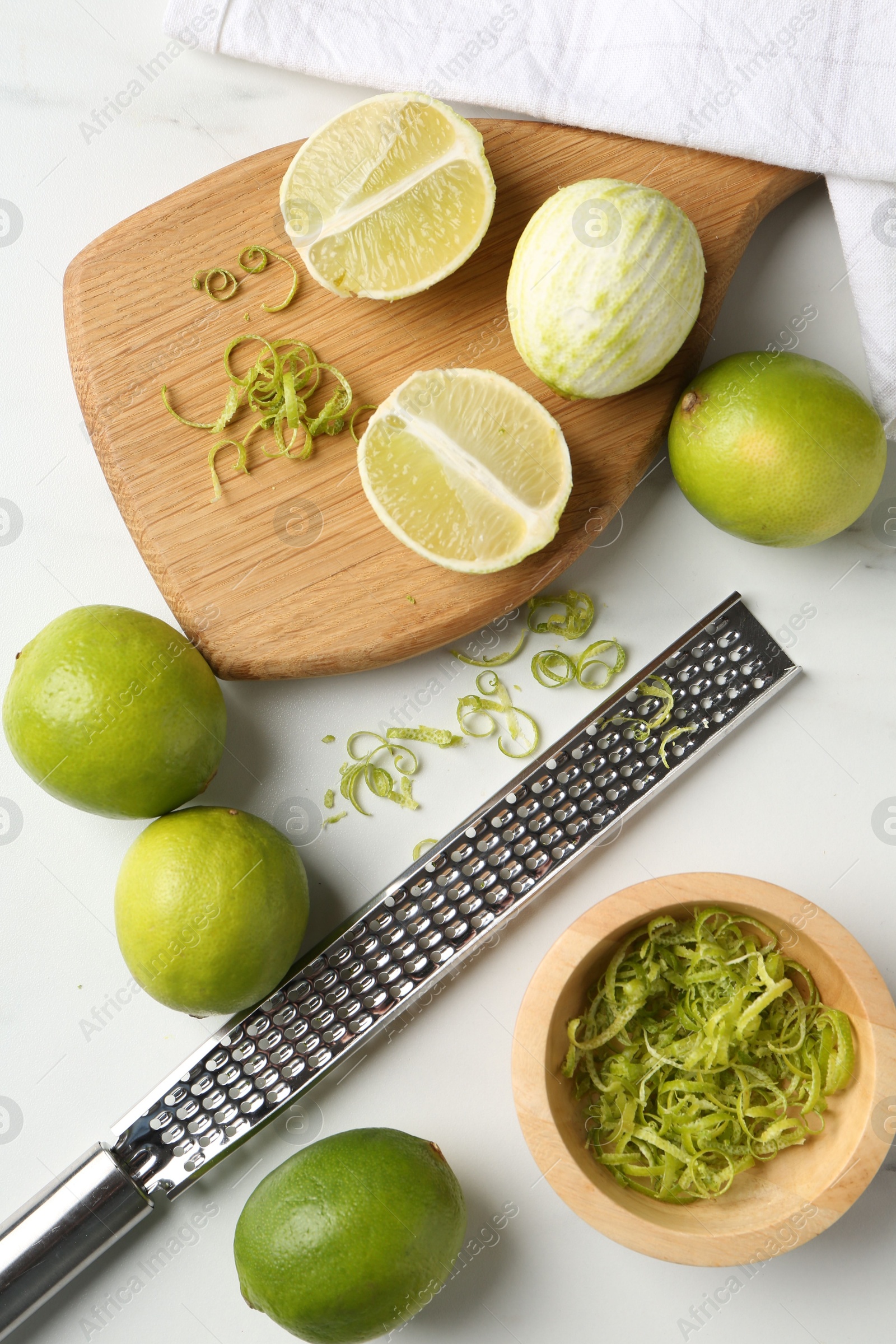 Photo of Lime zest, fresh fruits and grater on white marble table, flat lay