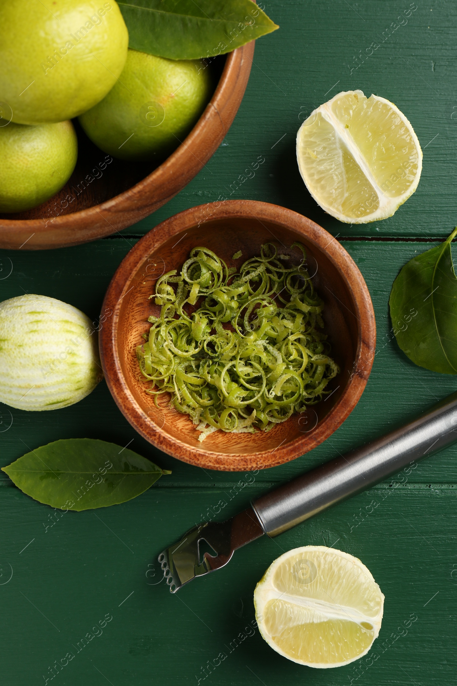 Photo of Lime zest, fresh fruits and zester tool on green wooden table, flat lay