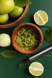 Photo of Lime zest, fresh fruits and zester tool on green wooden table, flat lay