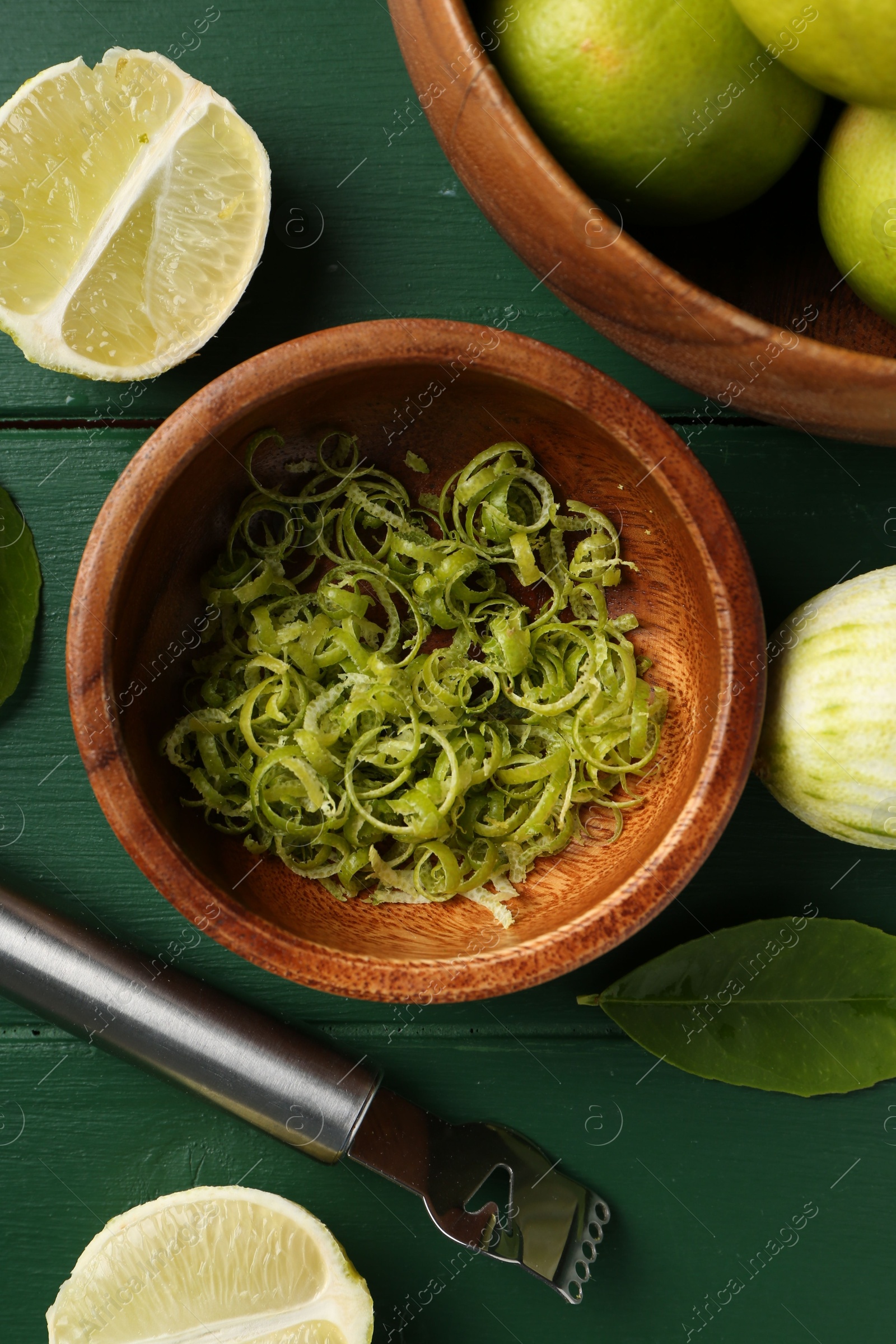 Photo of Lime zest, fresh fruits and zester tool on green wooden table, flat lay