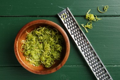 Photo of Lime zest in bowl and grater on green wooden table, flat lay