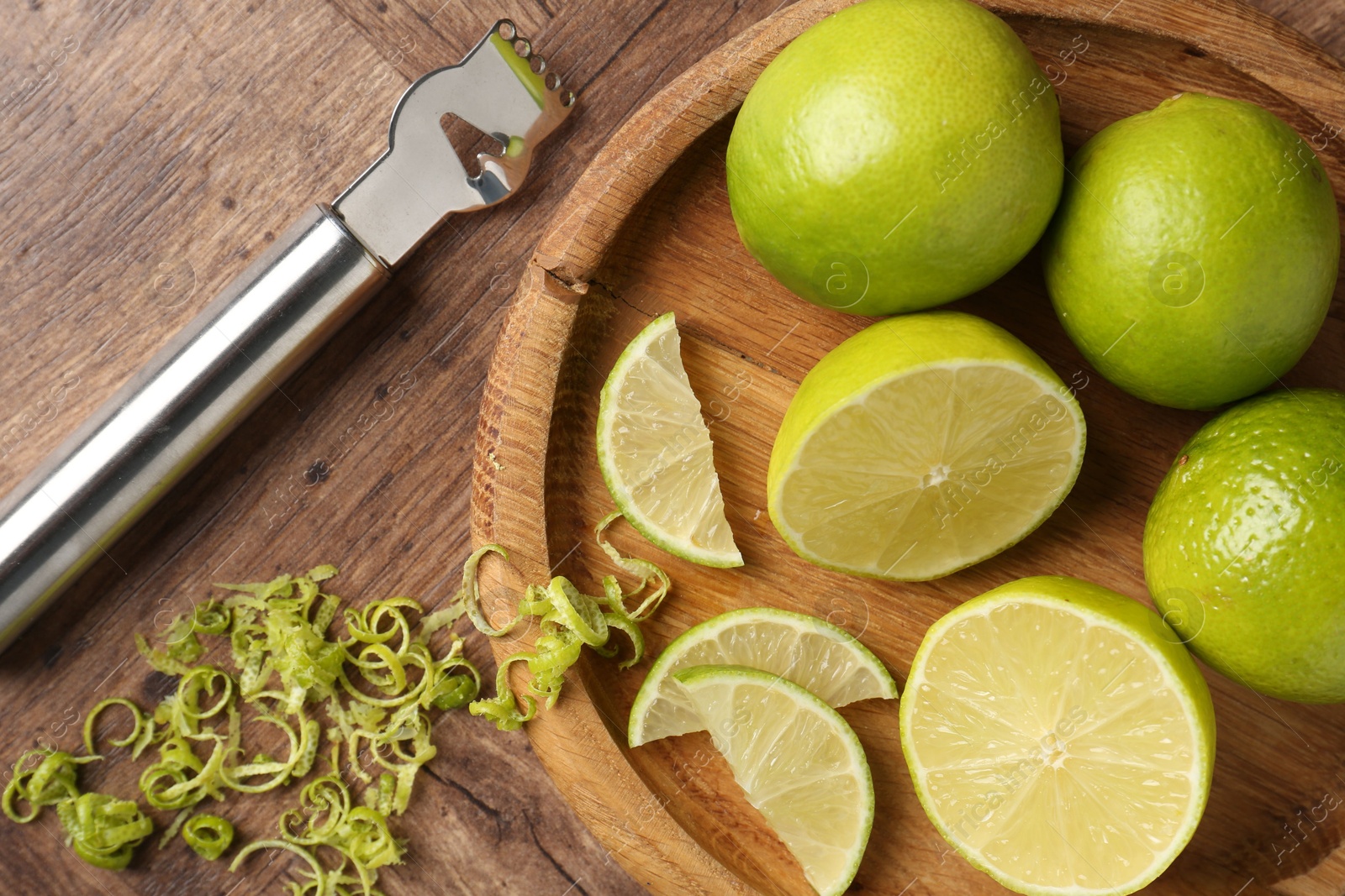 Photo of Lime zest, fresh fruits and zester tool on wooden table, flat lay