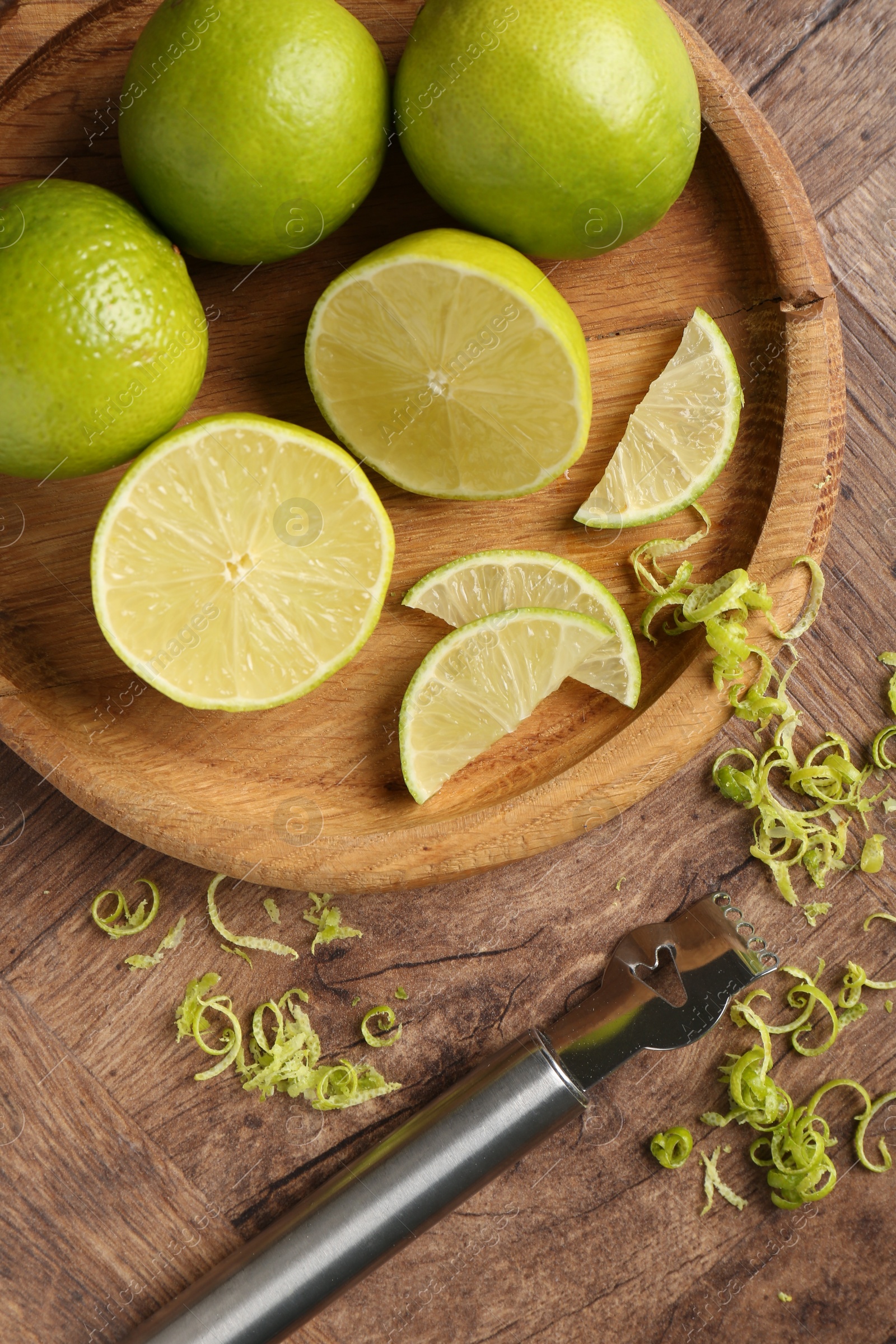 Photo of Lime zest, fresh fruits and zester tool on wooden table, flat lay