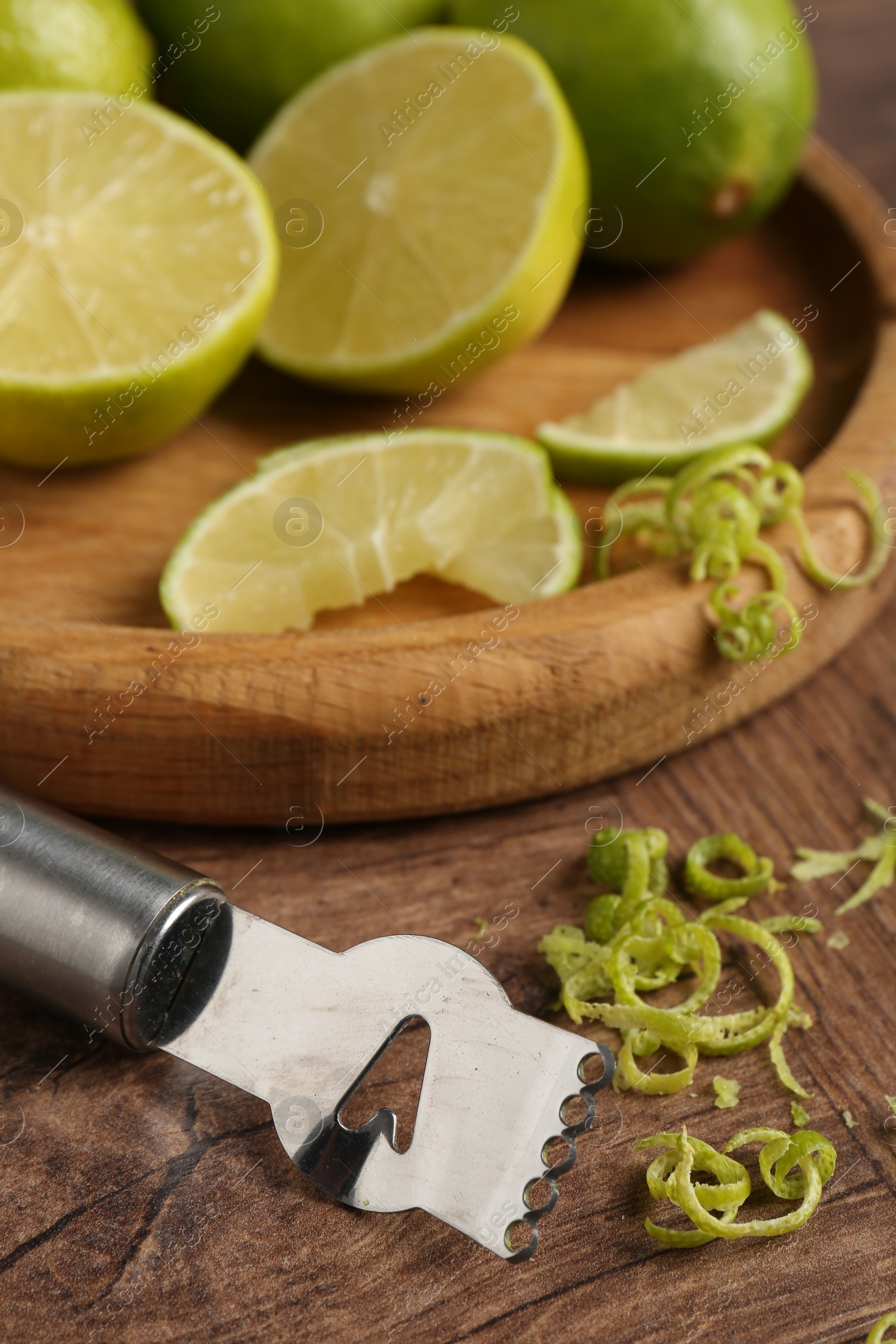 Photo of Lime zest, fresh fruits and zester tool on wooden table, closeup