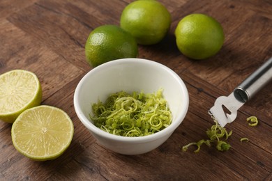 Photo of Lime zest in bowl, fresh fruits and zester tool on wooden table