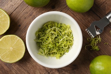 Photo of Lime zest in bowl, fresh fruits and zester tool on wooden table, flat lay