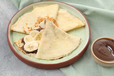 Photo of Delicious crepes with chocolate sauce and banana on grey table, closeup