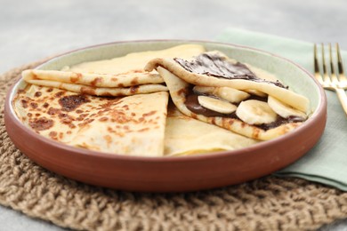 Delicious crepes with chocolate sauce and banana on grey table, closeup