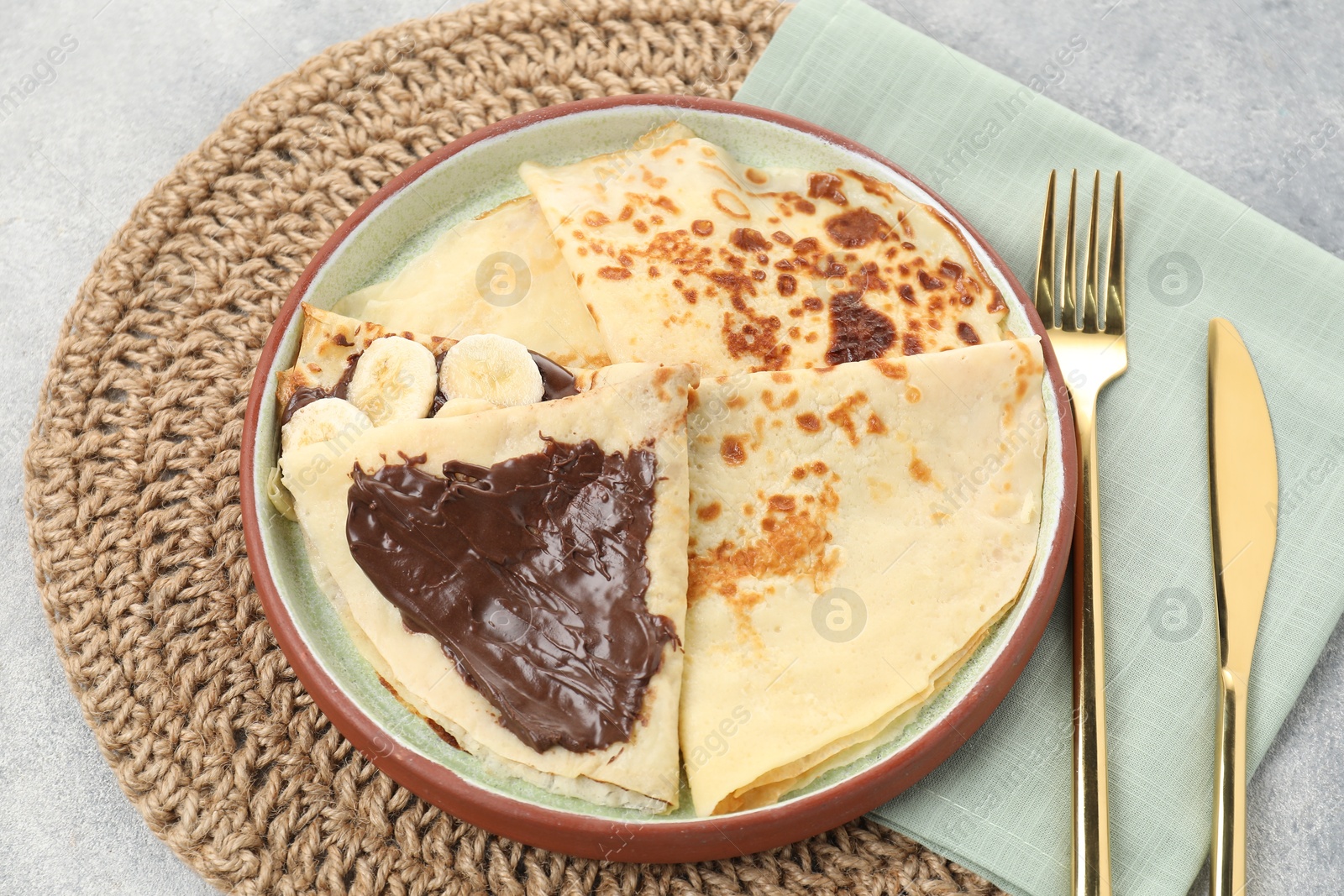 Photo of Delicious crepes with chocolate sauce and banana served on grey table