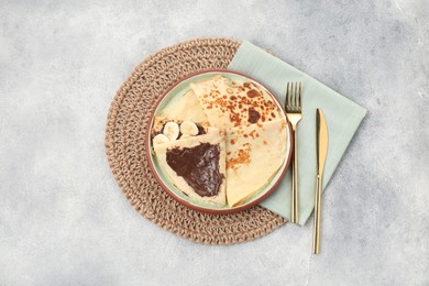 Delicious crepes with chocolate sauce and banana on grey table, top view