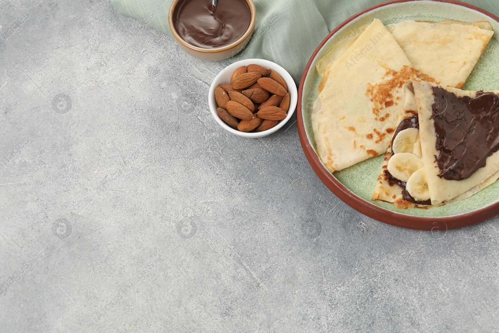 Photo of Delicious crepes with chocolate sauce and banana served on grey table. Space for text