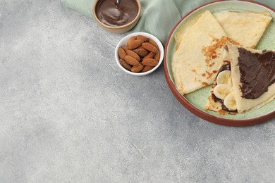 Photo of Delicious crepes with chocolate sauce and banana served on grey table. Space for text