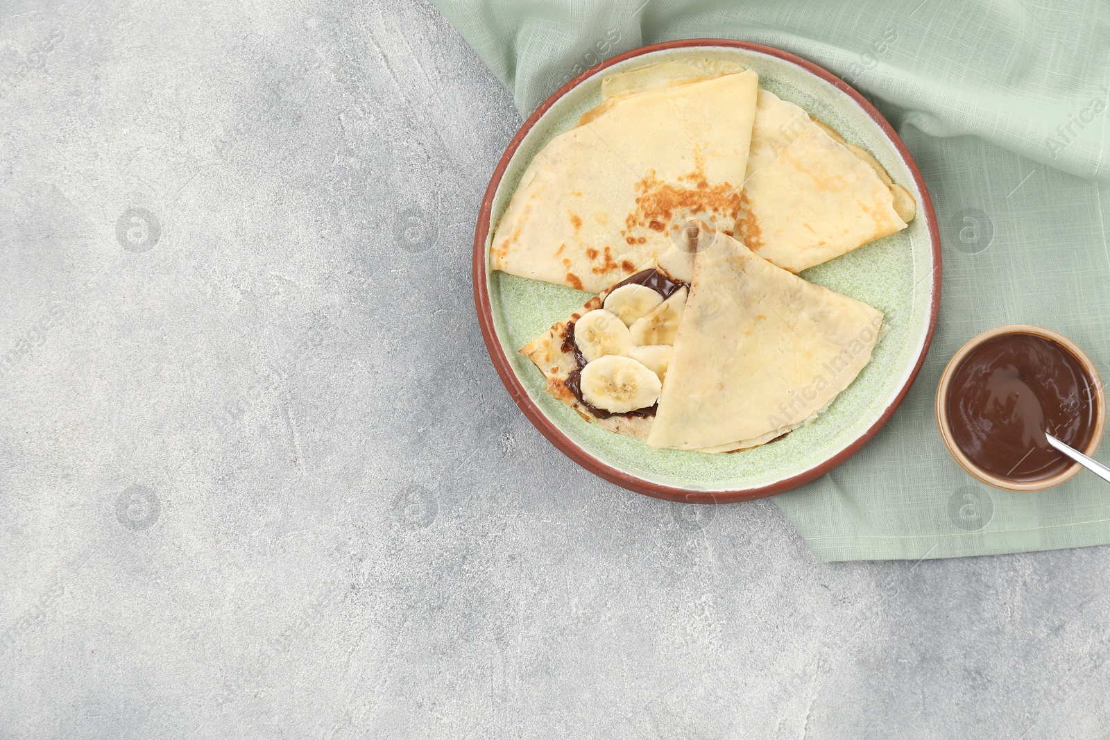 Photo of Delicious crepes with chocolate sauce and banana on grey table, top view. Space for text