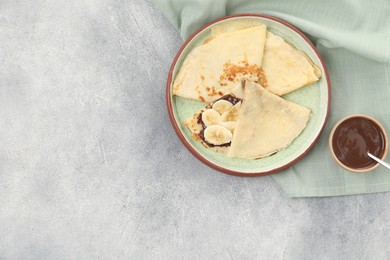 Delicious crepes with chocolate sauce and banana on grey table, top view. Space for text