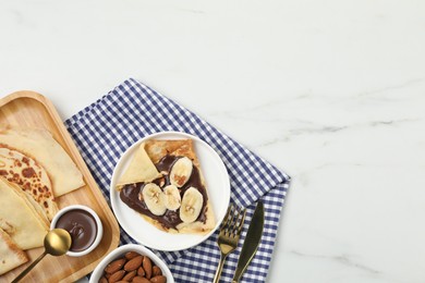 Photo of Delicious crepes with chocolate sauce, banana and almonds served on white table, flat lay. Space for text