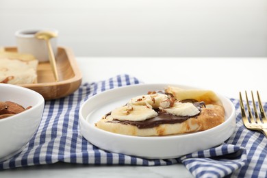 Photo of Delicious crepes with chocolate sauce, banana and almonds served on white table, closeup