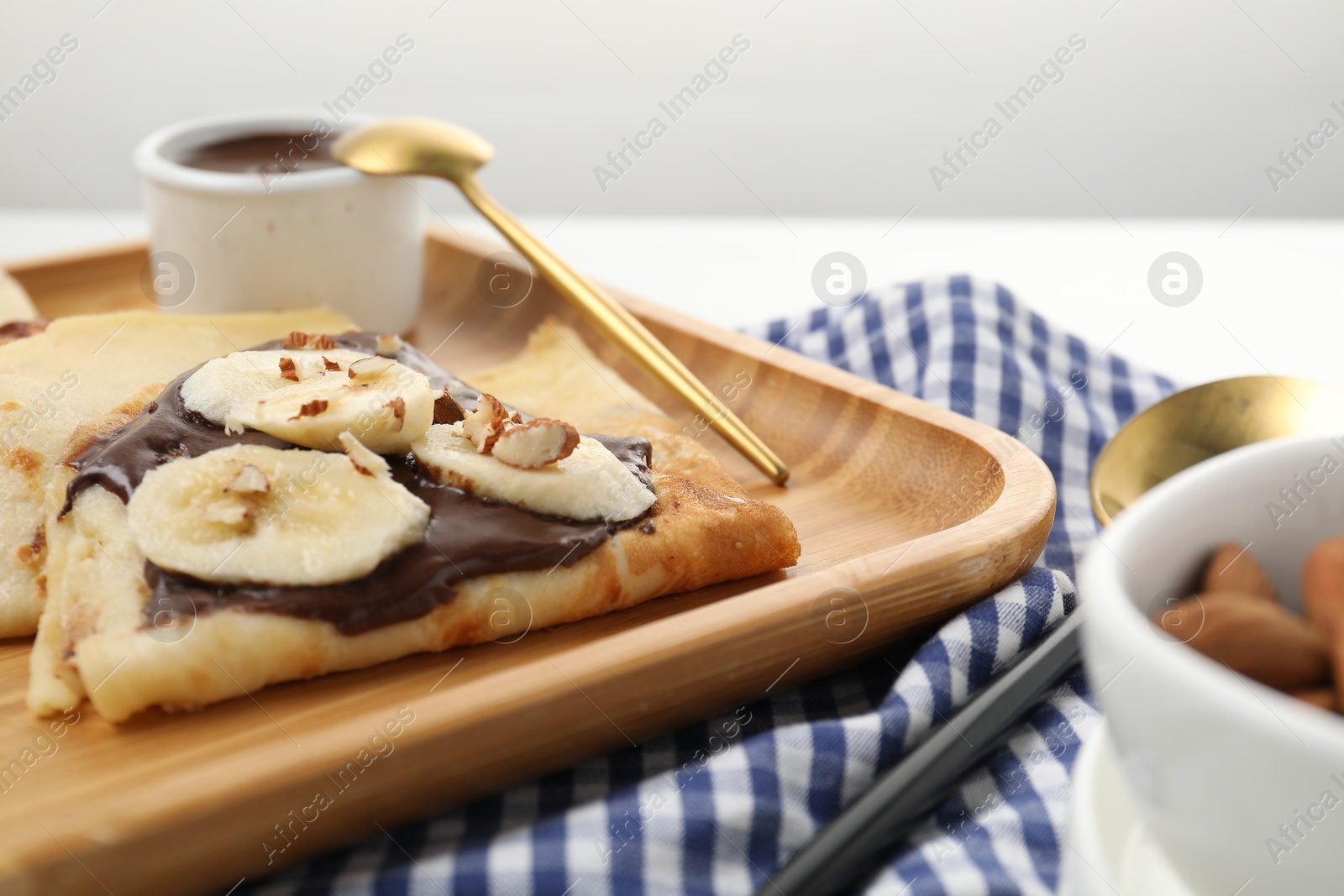 Photo of Delicious crepes with chocolate sauce, banana and almonds served on white table, closeup