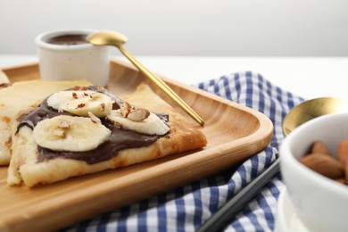 Photo of Delicious crepes with chocolate sauce, banana and almonds served on white table, closeup